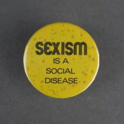 A yellow badge with black text that says sexism is a social disease.