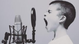 A photo of a young boy about 11 years old opening his mouth in front of a microphone. the background in neutral and the photograph is in black and white.