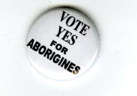 A white badge with black text that reads Vote Yes for Aborigines.