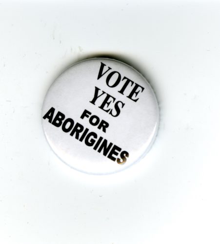 A white badge with black text that reads Vote Yes for Aborigines.
