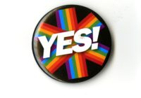 A badge with white text that reads YES. There is a six pringed rainbow star behind the text and a black background.