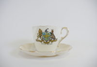 A small white teacup and saucer with the coat of arms for Adelaide City Council on the front.