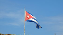 A photo of the Cuban flag including a red triangle with a white star inside and blue and white stripes.