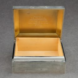 A small silver box with an open lid. The inside of the box is made from wood.