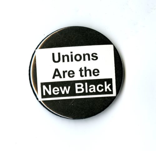 A black badge with a white square in the center. In the square is the phrase Unions are the New Black.