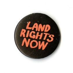 A black badge with red text that says LAND RIGHTS NOW.